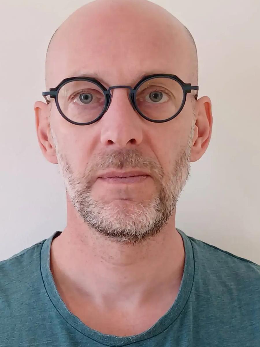 Portrait d'Olivier Barontini, lunettes rondes, sur fond clair.